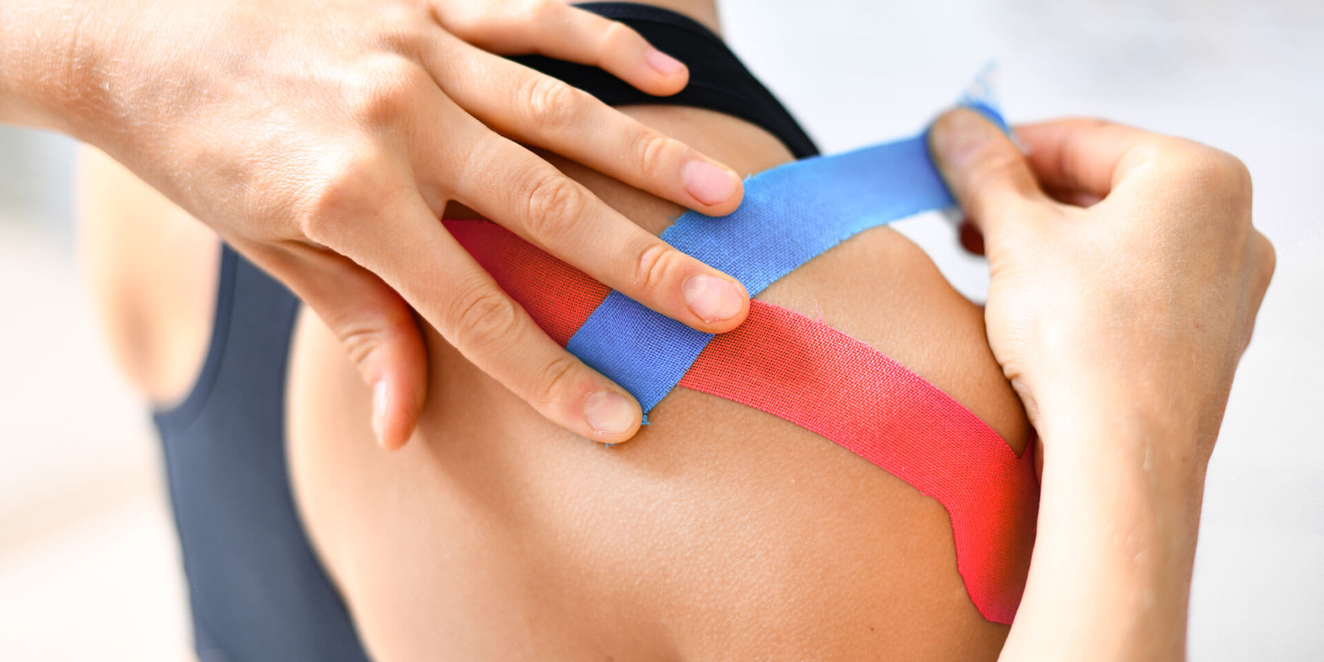 Behandlung mit blauen und rotfarbenen Kinesioband auf der verletzten Schulter einer Patienten.