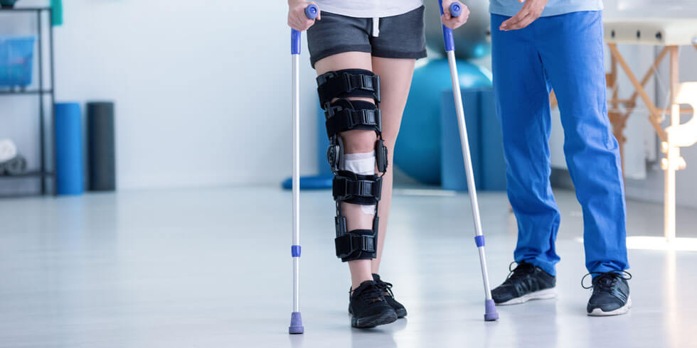 Sportphysiotherapeut und Patientin mit Beinverletzung während des Trainings mit Krücken