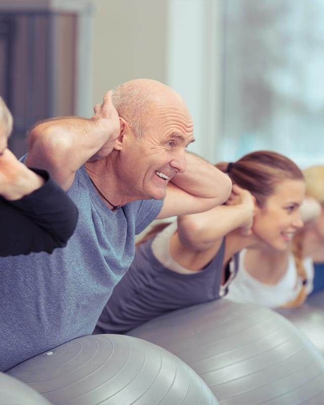 Rehasportklasse im Fitnessraum bei Rückenübungen mit Gymnastikball