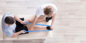 PhysiotherapeutIn trainiert mit Patienten mithilfe eines Gummibands die untere Beinmuskulatur