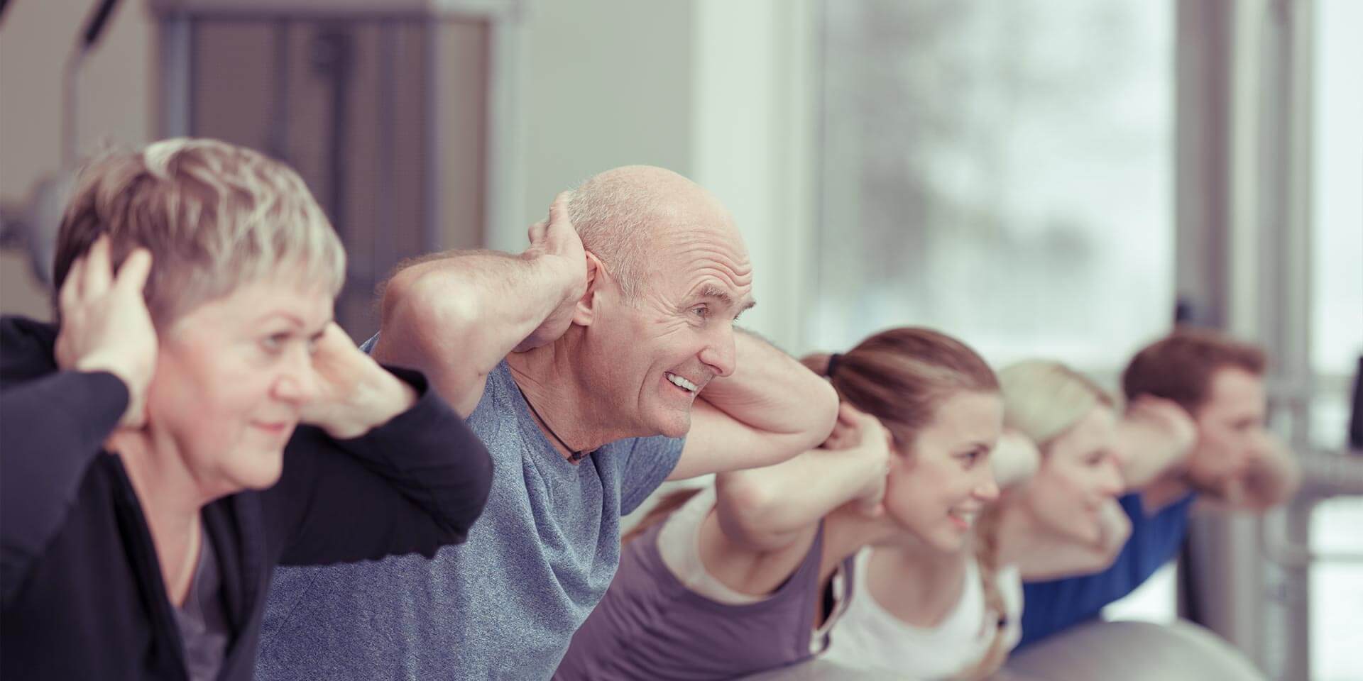 Rehasportklasse im Fitnessraum bei Rückenübungen mit Gymnastikball