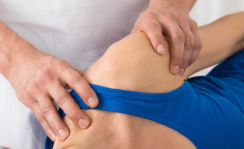 Physiotherapeut massiert Schulter einer Patientin