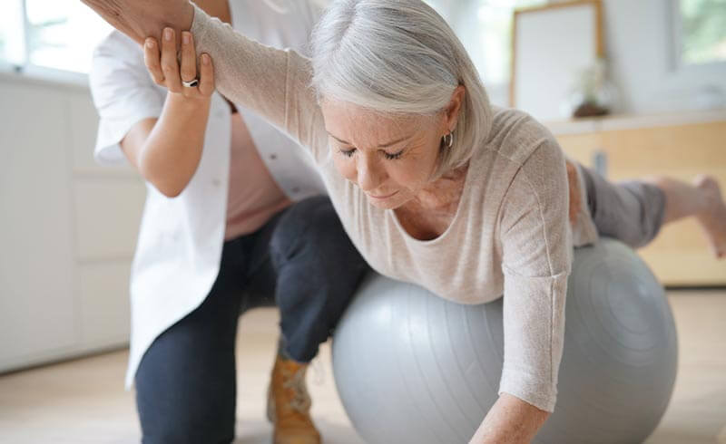 ältere Dame trainiert Gleichgwicht mithilfe eines Gymnastikballs